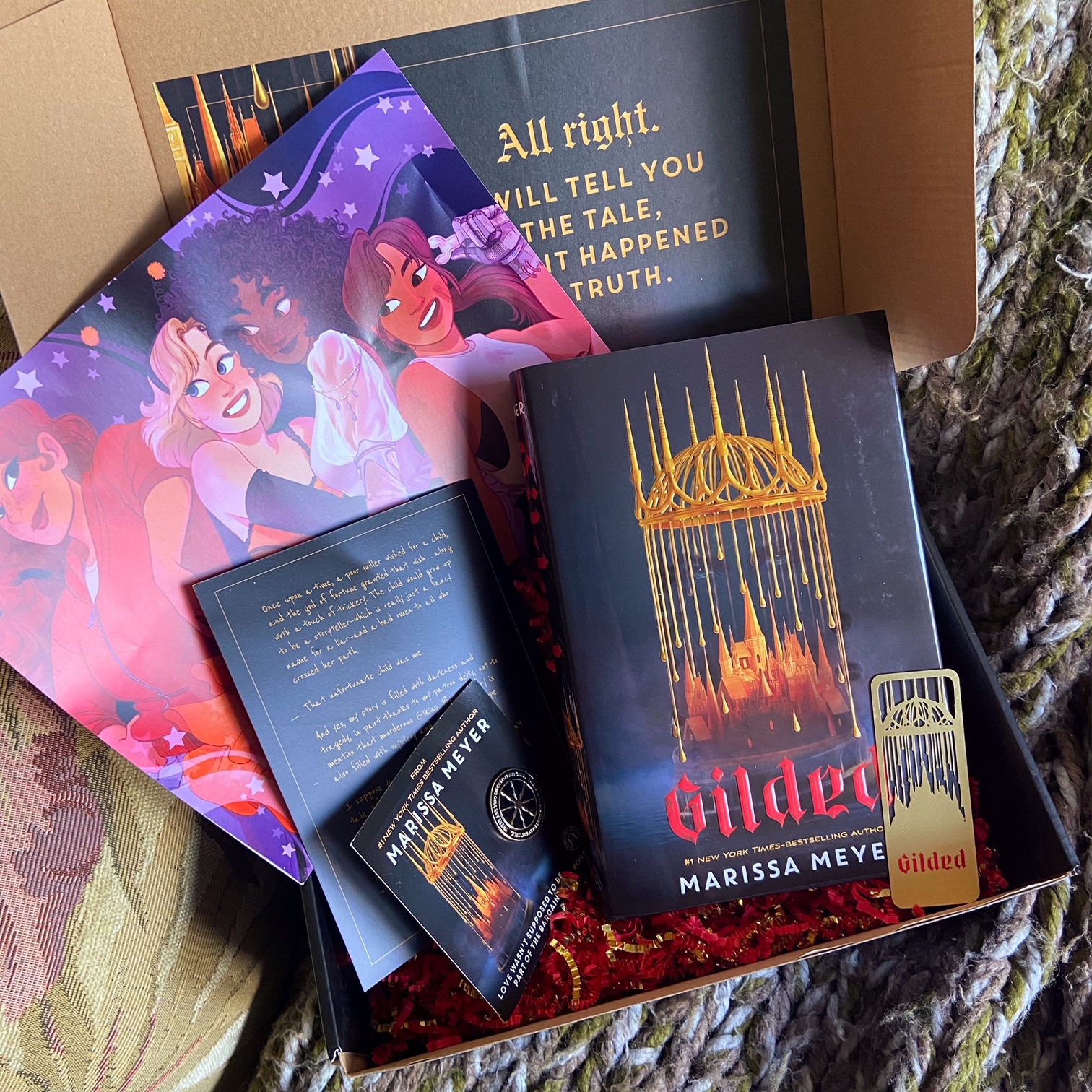 a photo of the Gilded promotional box, including a hardcover copy of Gilded, a character art poster, an enamel pin, a metal bookmark, and a note from Marissa Meyer about the book
